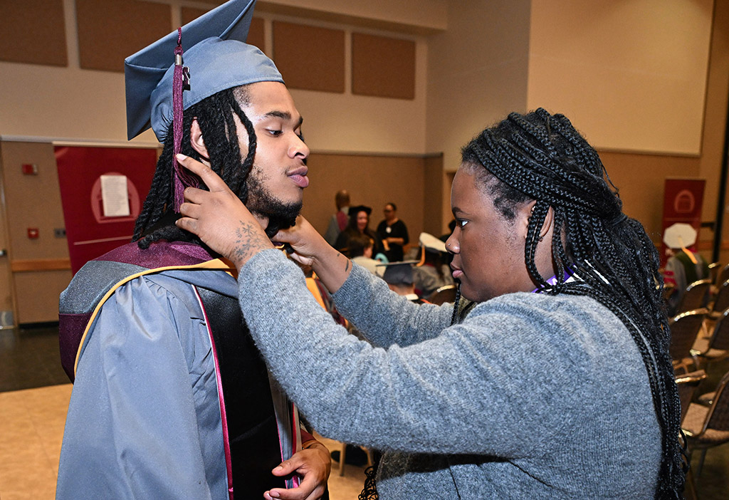 SANS Pre-Vet graduate Tyler Simmons gets help from Logan Quinn during the 139th Spring Commencement.