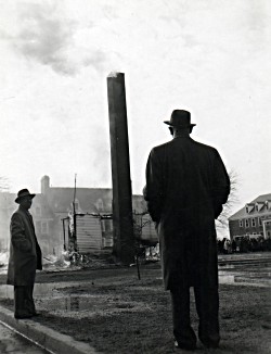 Two men observe the smoldering remains of DelCon Hall.