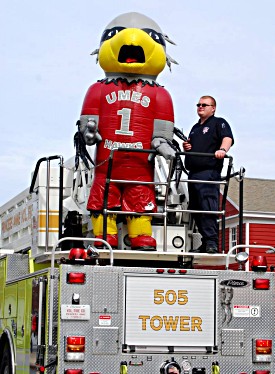 Harry the Hawk rides on top of a firetruck with a first responder