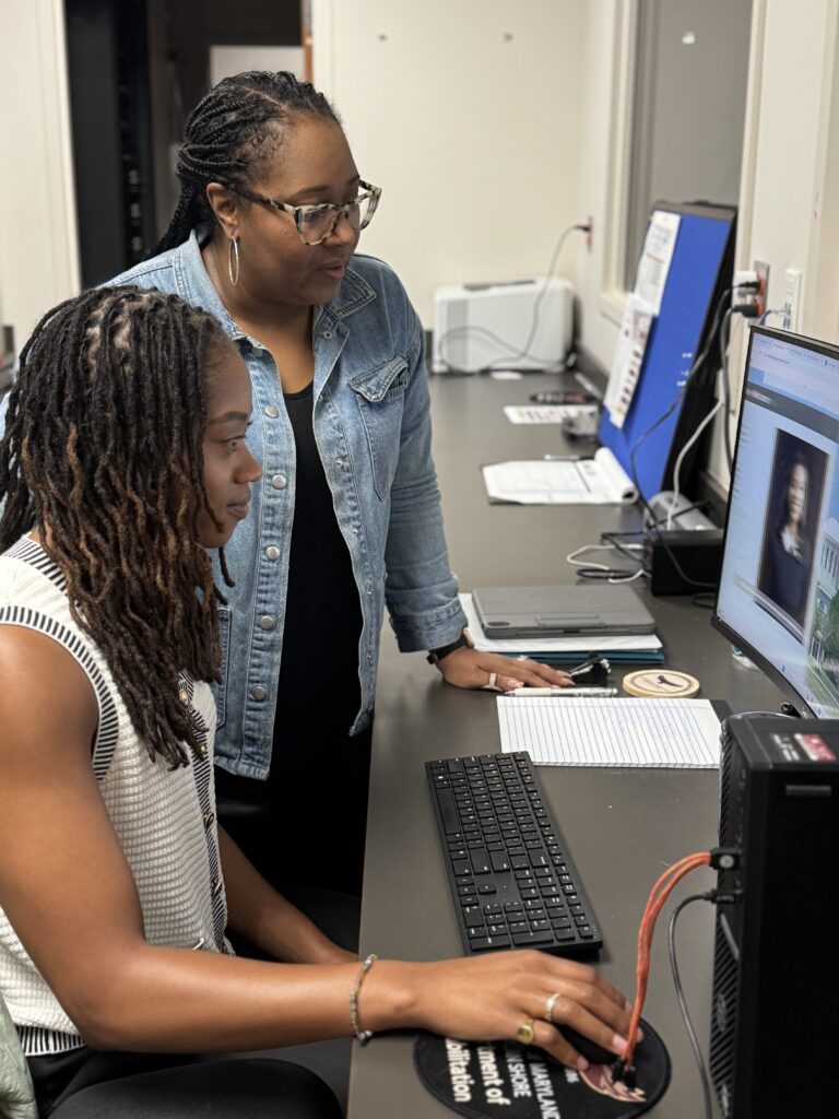 Staff member supports a student at a computer workstation during an advising activity.